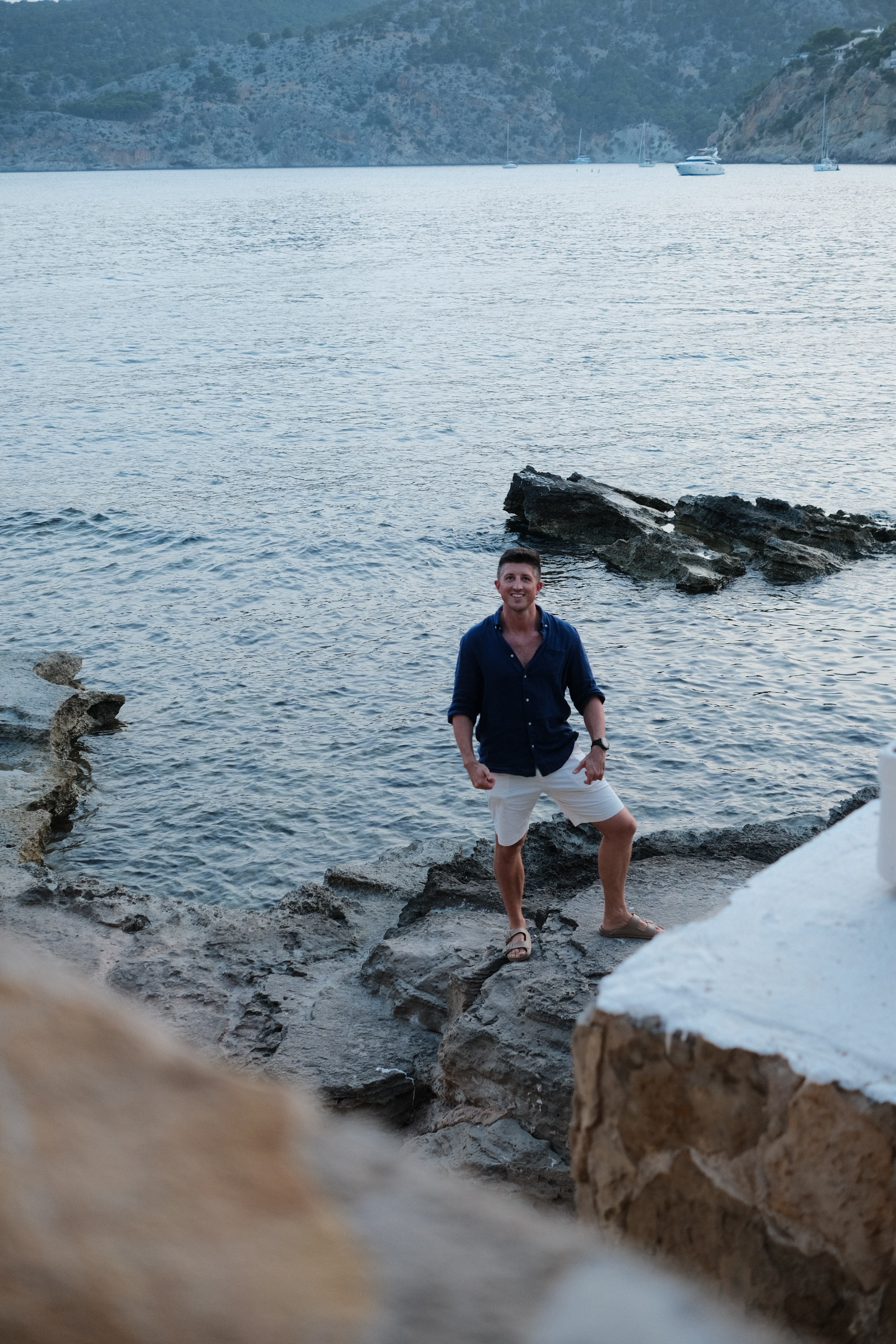 Will, founder of MYKINDREDCREW, standing beside a Mediterranean cove with yachts at anchor